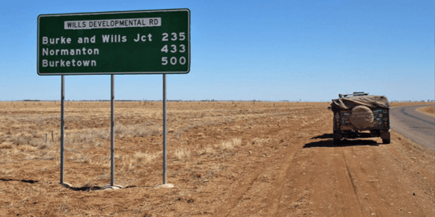 Wills Developmental Road distance sign beside the narrow sealed road through dry outback grassland