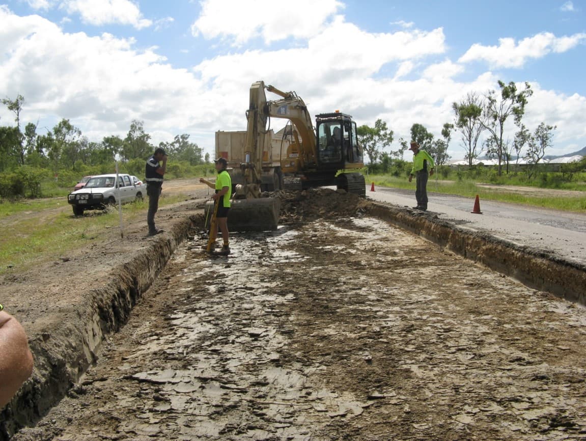 Excavator and crew excavating the pavement on Dalrymple Road beside an open traffic lane